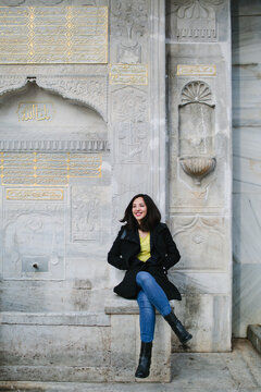 Smiling Uzbek woman sits on an Ottoman fountain in Istanbul.