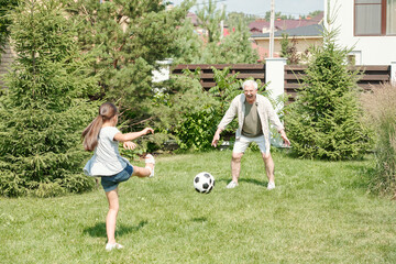 Active senior man playing soccer with his little granddaughter on lawn in backyard, copy space © pressmaster