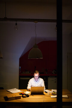 Young man working overtime in a dark office behind his laptop