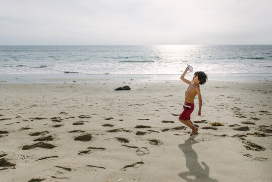 boy runs along the seashore with a paper airplane ready to launch