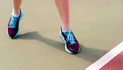 Legs of young girl in a closed tennis court with racket, sport shoes