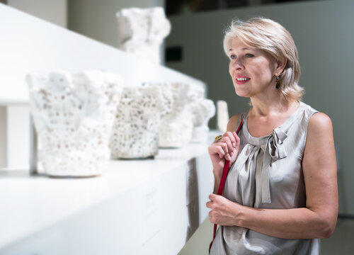 Mature woman standing in museum near the antique sculpture