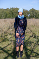 Naklejka na ściany i meble Portrait of a cheerful woman in a knitted hat, coat, pretty dress and boots, smiles cute, poses, smiles on yellow field. The concept of rustic style and life in ancient times
