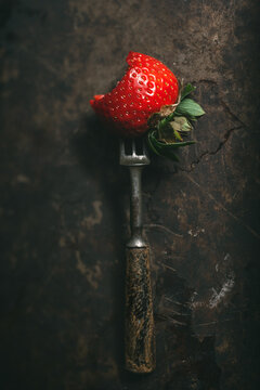 Half eaten strawberry on an old fork against a metal background.