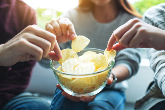 Closeup image of friends sharing and eating potato chips at home party together