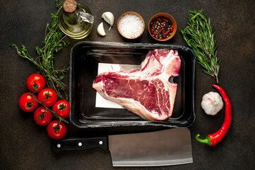 raw t-bone steak vacuum packed with
ingredients on stone background