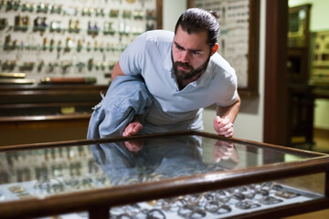 Adult man looking at exhibits in glazed stands in historical museum. High quality photo