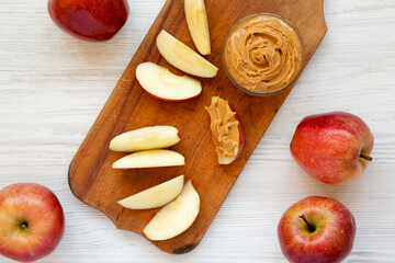 Raw Red Apples and Peanut Butter on a rustic wooden board on a white wooden background, top view. Flat lay, overhead, from above.