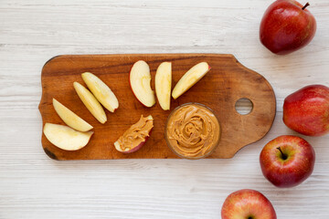 Raw Red Apples and Peanut Butter on a rustic wooden board on a white wooden surface, top view. Flat lay, overhead, from above.