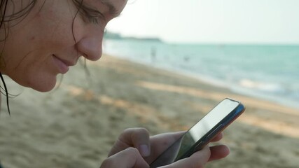 Female's Hands Using Black Smartphone on Sea Water Background. Gadget concept. Reading text message. Waves surface background on sandy beach