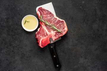 raw t-bone steak with ingredients on a meat knife on stone  background