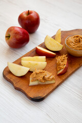 Raw Red Apples and Peanut Butter on a rustic wooden board on a white wooden surface, side view.