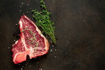 
raw t-bone steak with ingredients on stone background with copy space for your text
