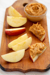 Raw Red Apples and Peanut Butter on a rustic wooden board on a white wooden surface, low angle view.