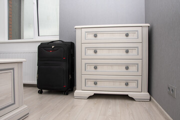 Minimalistic interior of the room with a chest of drawers and a suitcase on the wooden floor. Concept: hotel accommodation for visitors, hotel room for tourists, home interior.