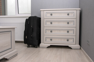 Minimalistic interior of the room with a chest of drawers and a suitcase on the wooden floor. Concept: hotel accommodation for visitors, hotel room for tourists, home interior.