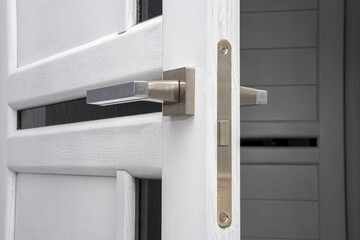 Fototapeta na wymiar Open interior white wooden door with metal handle, close-up, modern design.
