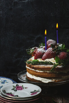 Strawberry and cream genoise sponge cake with two candles in low light.