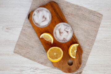 Fresh Lemon Sparkling Water with Ice on a rustic wooden board, overhead view. Top view, from above, overhead.