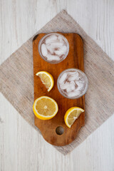 Fototapeta na wymiar Fresh Lemon Sparkling Water with Ice on a rustic wooden board on a white wooden background, overhead view. Top view, from above, flat lay.
