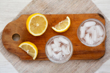 Fresh Lemon Sparkling Water with Ice on a rustic wooden board, top view. Overhead, from above.