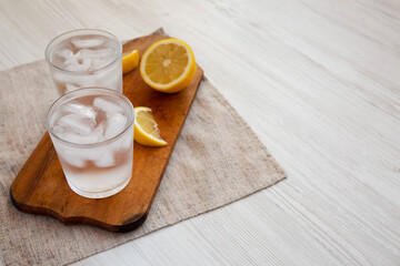 Fresh Lemon Sparkling Water with Ice on a rustic wooden board, side view. Copy space.