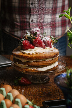Strawberry and cream sponge being dusted with icing sugar.