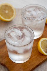 Fresh Lemon Sparkling Water with Ice on a rustic wooden board, side view.