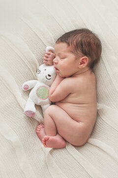Newborn baby sleeping with a white plush bunny toy.