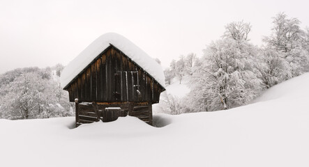 Minimalistic winter landscape with wooden house in snowy mountains. Cloudy weater, landscape photography