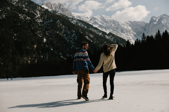 Old sweater couple walking towards snowy mountains