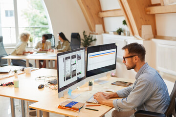 Serious programmer sitting at his workplace using computers in his work he developing new software...