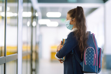 Schoolgirl in a protective mask with a backpack and a textbook in her hands. Security concept, virus protection. Covid-2019.