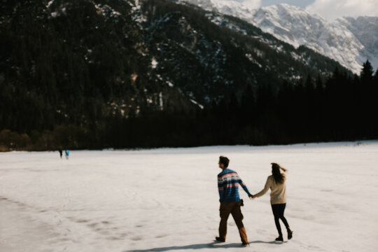 Couple holding hands walking over frozen lake