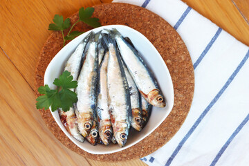 Fresh raw sardines in a bowl with parsley leaves on wooden table. Sardina pilchardus
