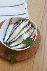 Fresh raw sardines in a bowl with parsley leaves on wooden table. Sardina pilchardus
