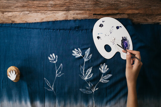Artist Painting White Flowers on a Blue Fabric