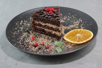 Piece of chocolate cake on a black plate with berries and mint leaves