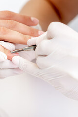 Hands of manicurist pushing cuticles on female's nails with manicure tool. Woman receiving manicure and nail care procedure