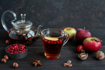 Warming hot tea in a glass cup and kettle. Snack with tea, apples, berries and nuts on a black wooden background.