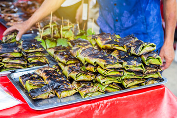 Traditional thai food grill marinate fish wraping with banana leaves, food market in Thailand,...