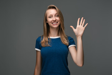 Fototapeta na wymiar Cheerful girl with blonde straight hair waving raised palm. Say HELLO. Human emotions, facial expression concept.