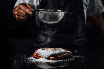 Confectionery Chef making sweets, Man hands sprinkle sweet sugar powder on cake dark background....