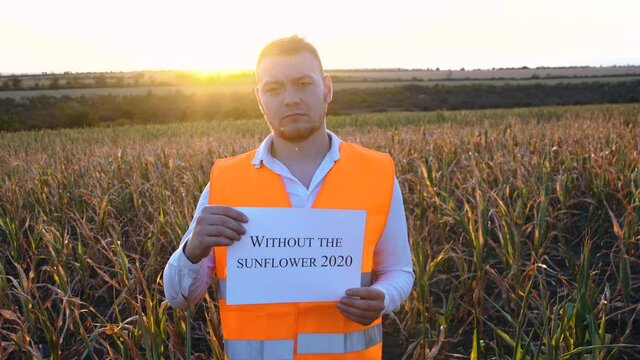 Portrait of a sad young farmer holding a plaque with the inscription No sunflower in 2020.