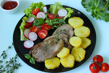 Baked beef tongue with fresh vegetables and potatoes on a black plate