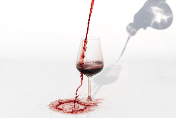 Sommelier pours red wine from decanter to wineglass on white background. spilling red wine past the glass on a white table.
