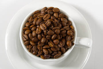 Coffee beans in white cup, close-up. White coffee cup with coffee seeds on white background. Concept For International day of coffee.