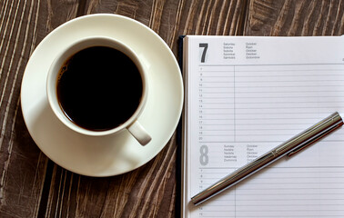 Open a blank white notebook, pen and cup of coffee on the wooden desk