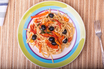 Vegetarian pasta with vegetables, linguine with bell pepper, tomatoes and olives on a plate - top view, close-up