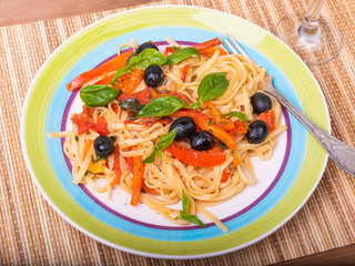 Vegetarian pasta with vegetables, linguine with bell pepper, tomatoes and olives on a plate standing on a napkin on the table - a close-up